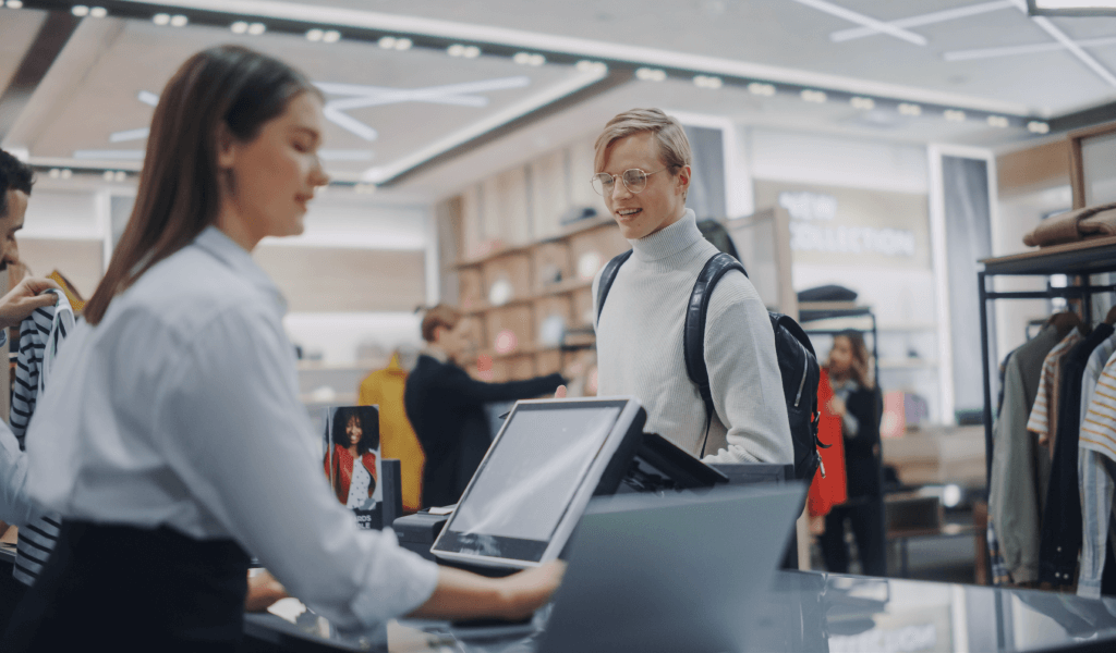 clothing-store-young-man-checkout-counter-buys-clothes-paying-with-contactless-nfc-smartphone-friendly-retail-sales-assistan-packs-merchandise-contemporary-fashion-shop-with-designer-brand