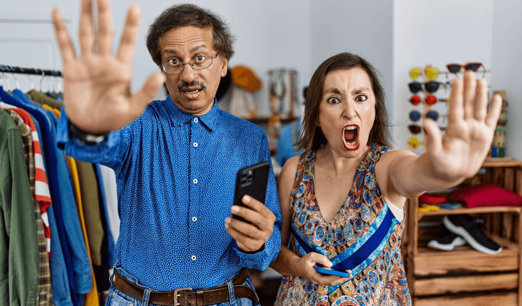 middle-age-interracial-couple-retail-shop-using-smartphone-doing-stop-gesture-with-hands-palms-angry-frustration-expression